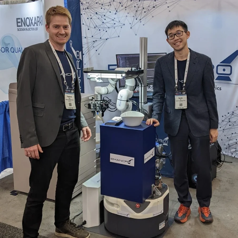 Emancro team members standing beside a medical robot at a trade show booth.
