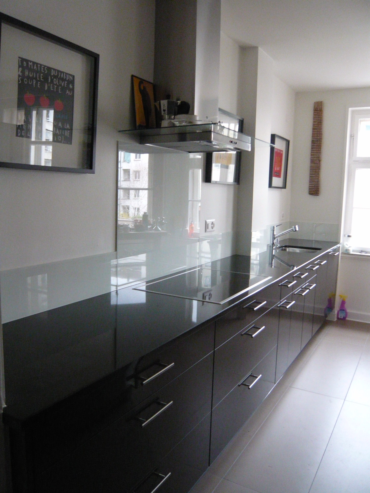 Modern kitchen with sleek black countertop, built-in stovetop, stainless steel hood, and sink near a window.