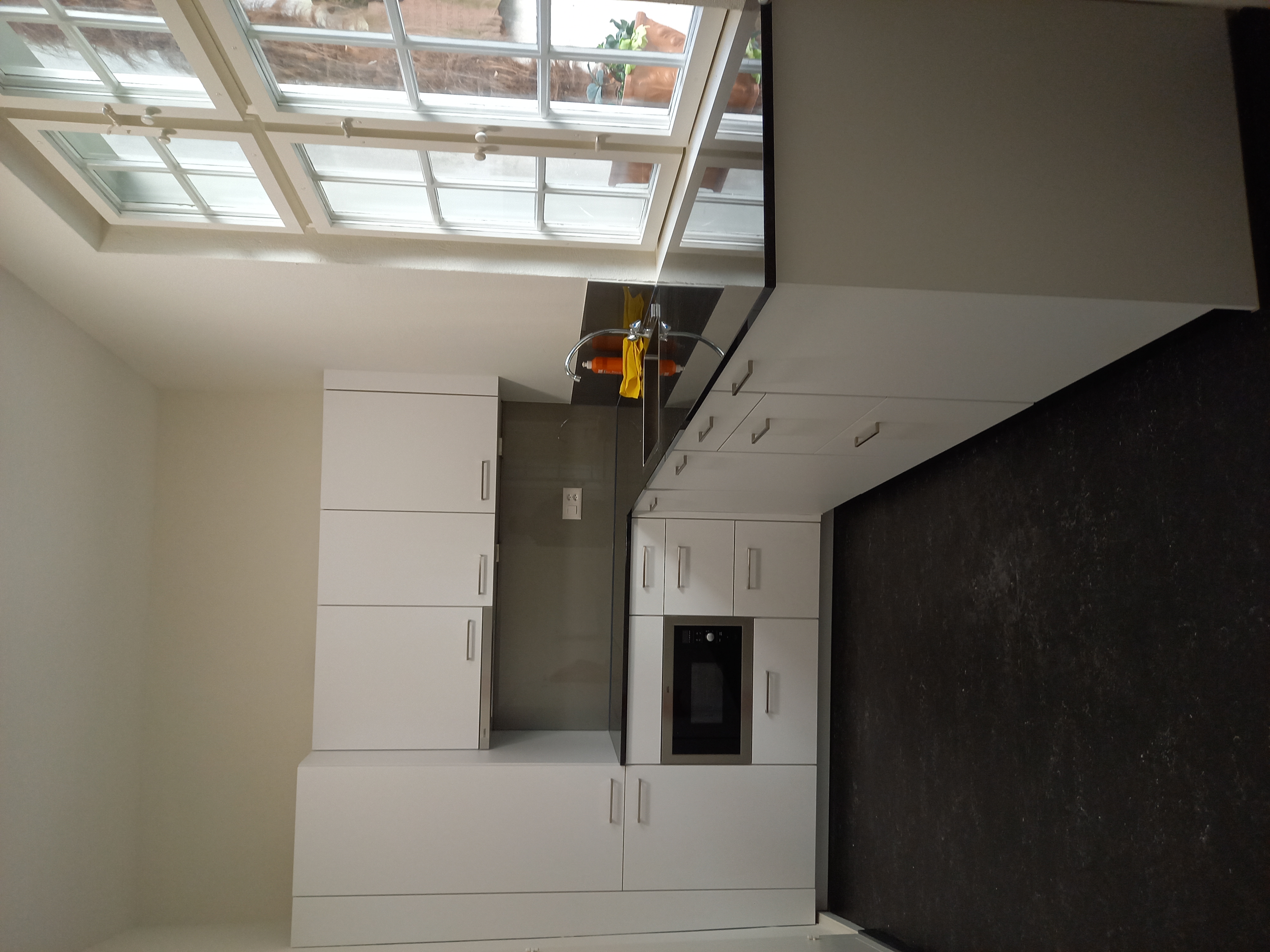 Small modern kitchen with white cabinets, black countertops, built-in microwave, and a window with potted plants outside.