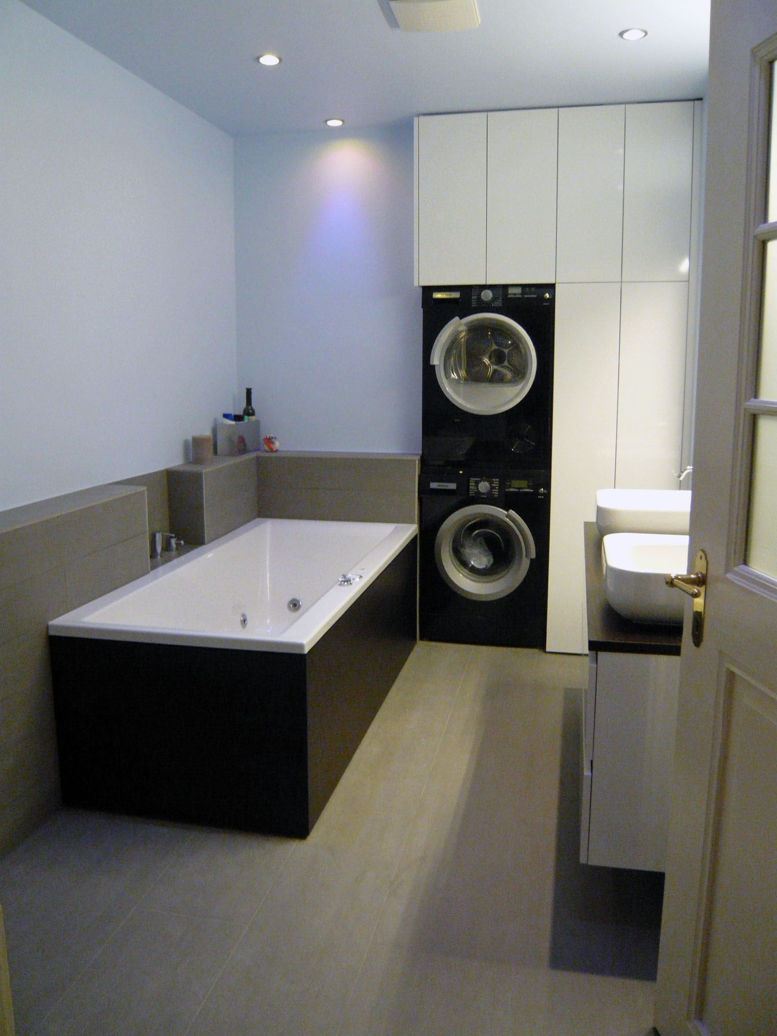 Modern bathroom with a black and white bathtub, stacked black washer and dryer, white cabinets, and two white sinks.