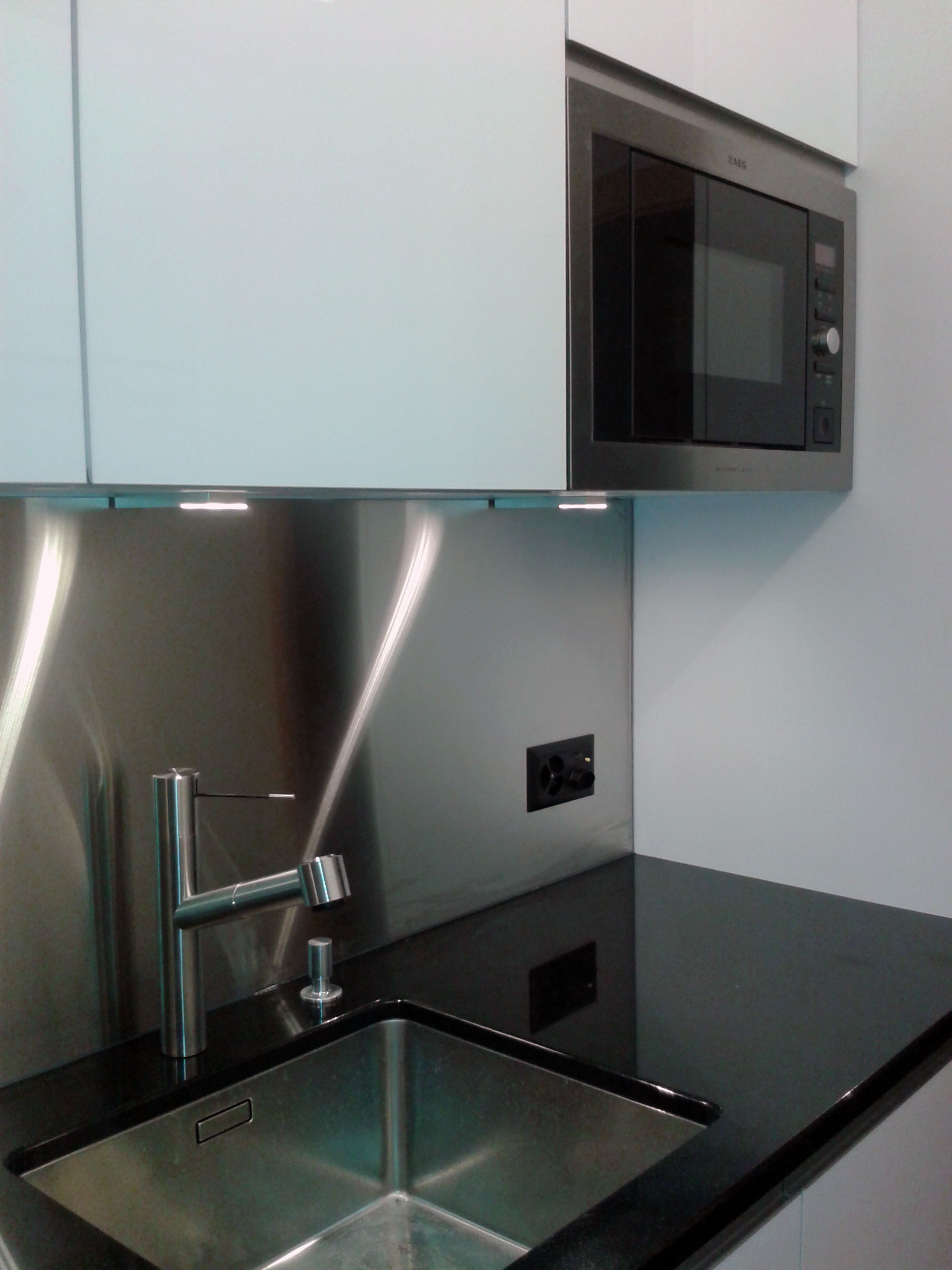 Modern kitchen sink with a stainless steel faucet, black countertop, and built-in microwave above.