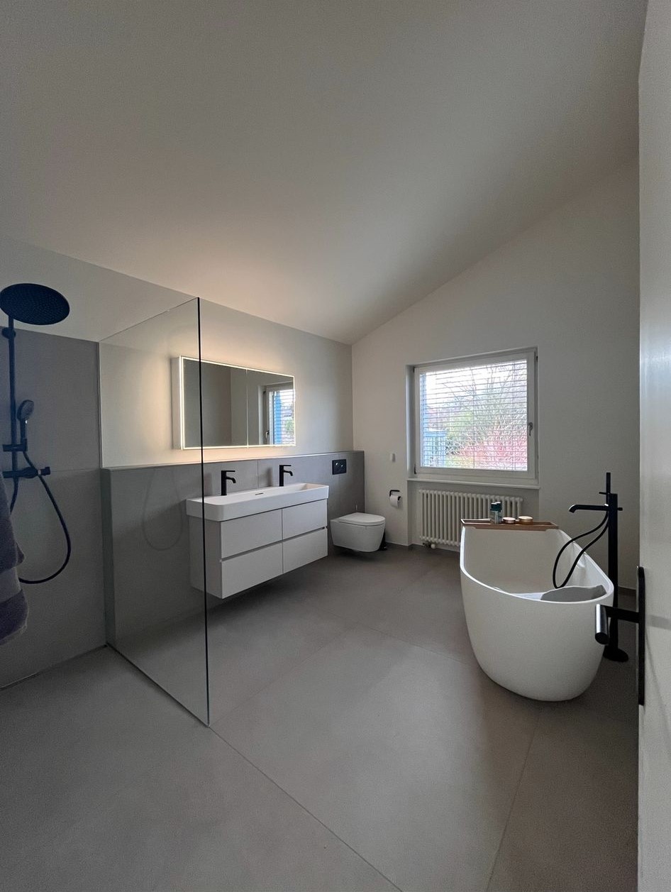 Modern bathroom with freestanding bathtub, walk-in shower with black fixtures, double sink vanity with illuminated mirror, and a window.