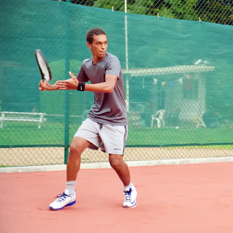 Young male tennis player preparing to hit a forehand shot on an outdoor clay court.