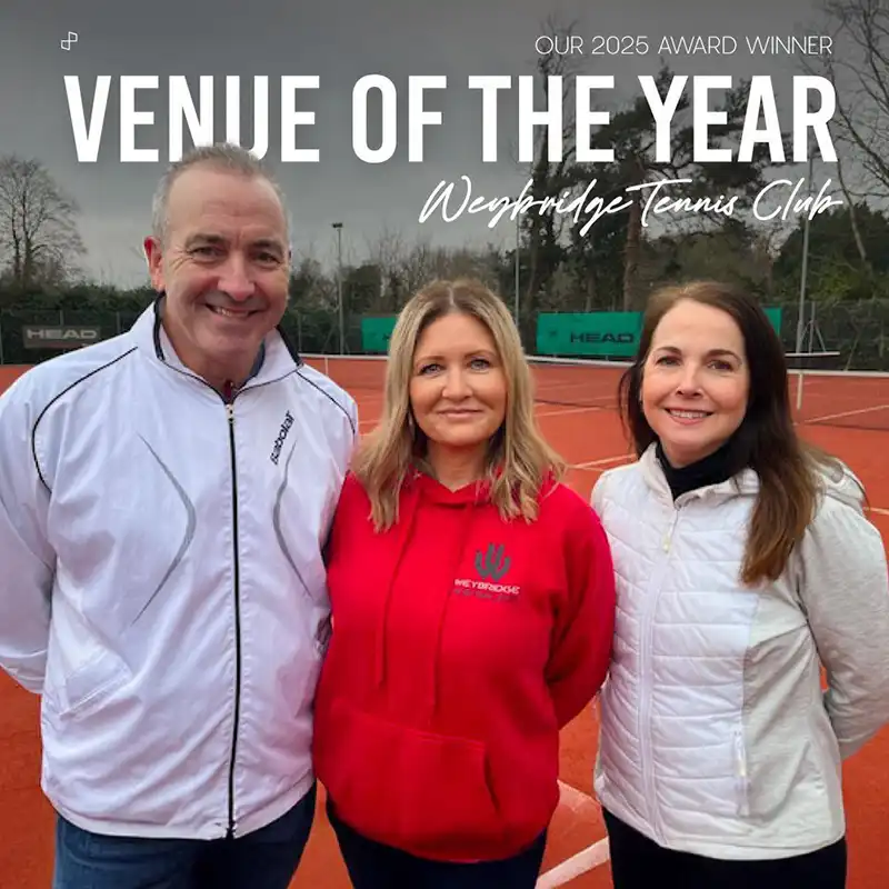 Three people standing on a clay tennis court smiling, with text above reading 'Our 2025 Award Winner Venue of the Year Weybridge Tennis Club'.