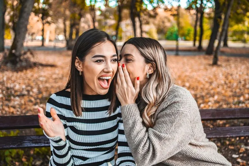Two women laugh as they sit on a bench.