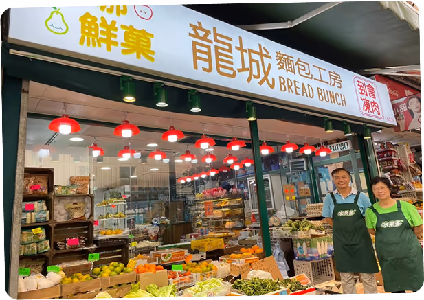 Staff members in green aprons working at Bread Bunch bakery counter with Chinese signage and display cases full of baked goods under warm lighting