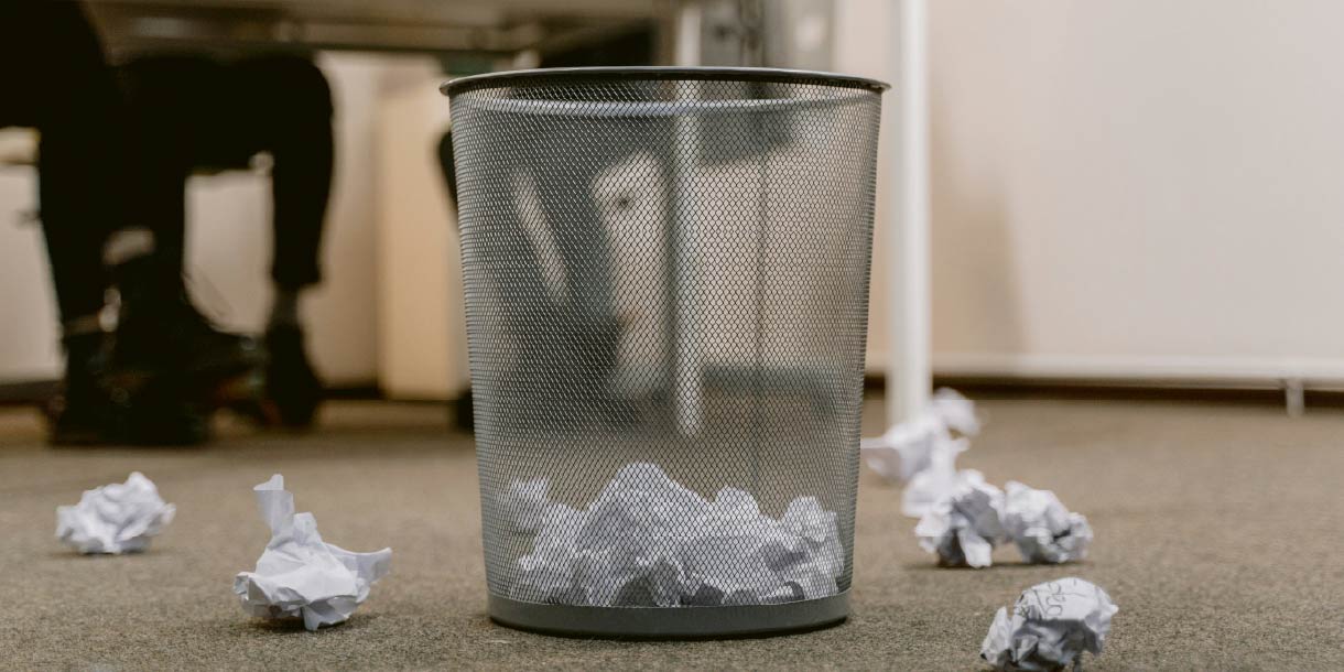 Trash can in office with white paper trash crumpled up in it and on the floor around it