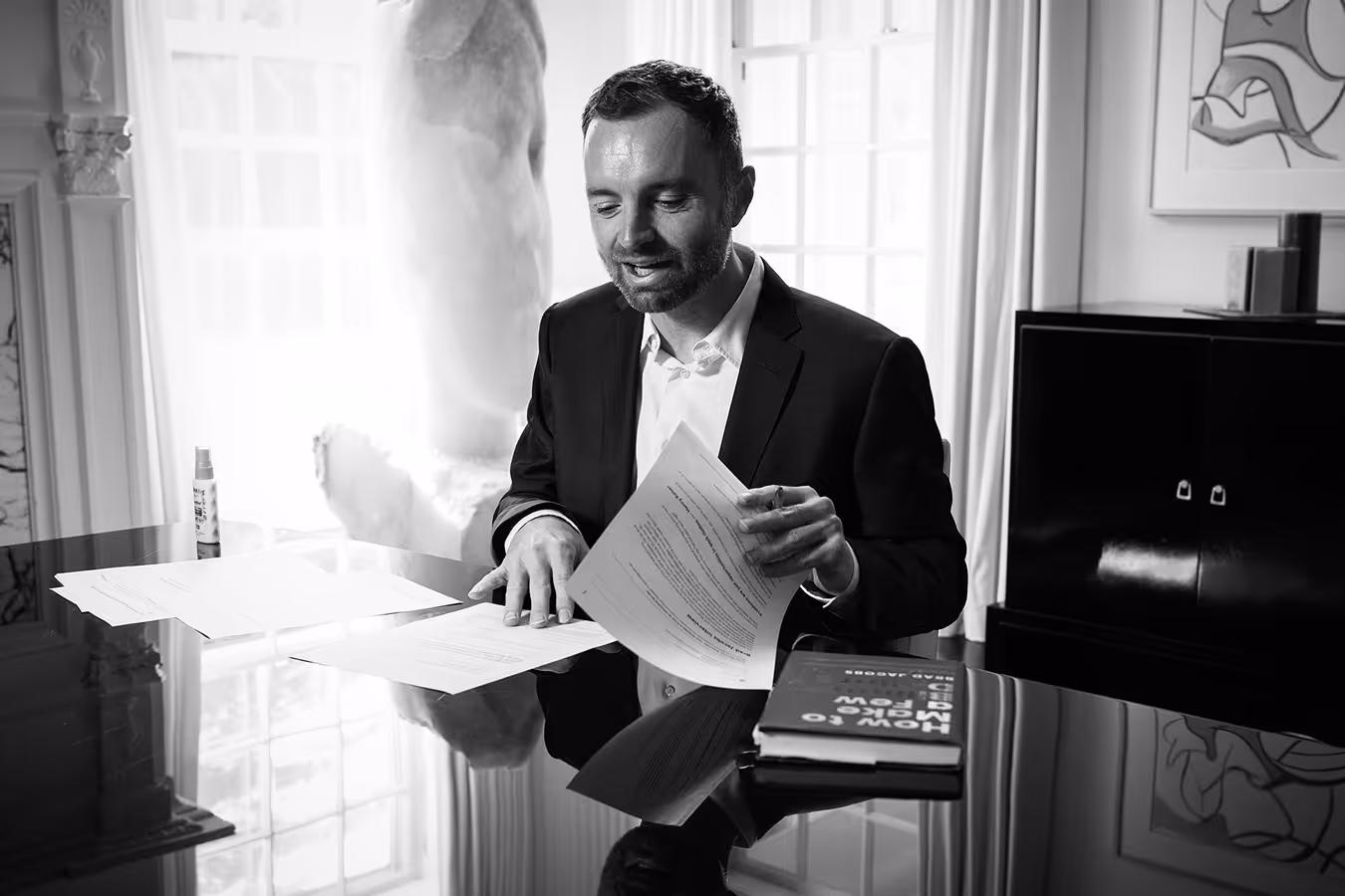 David Senra in a suit sits at a desk, focused on his work, with a professional demeanor.