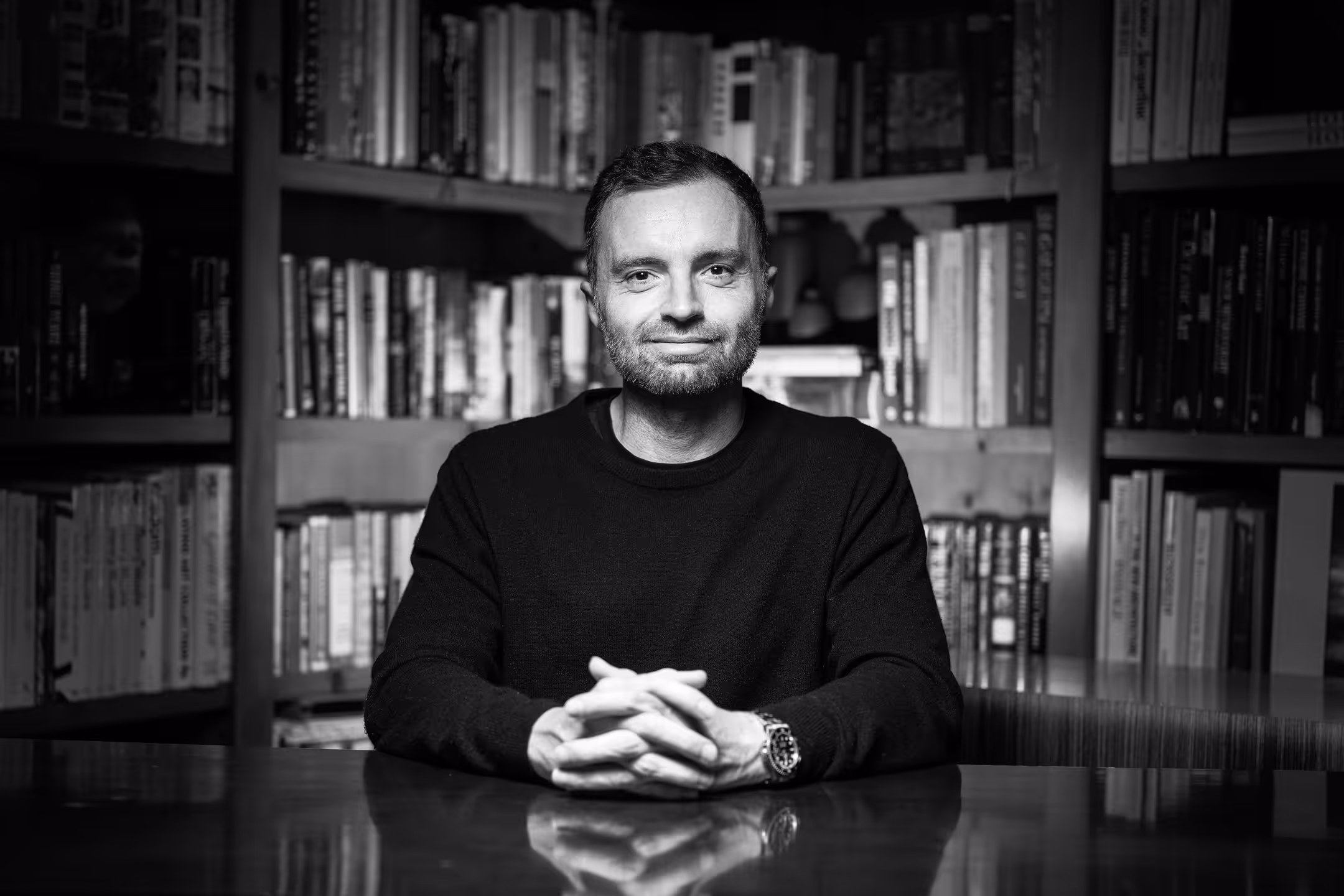 David Senra seated at a desk, surrounded by bookshelves filled with various books.