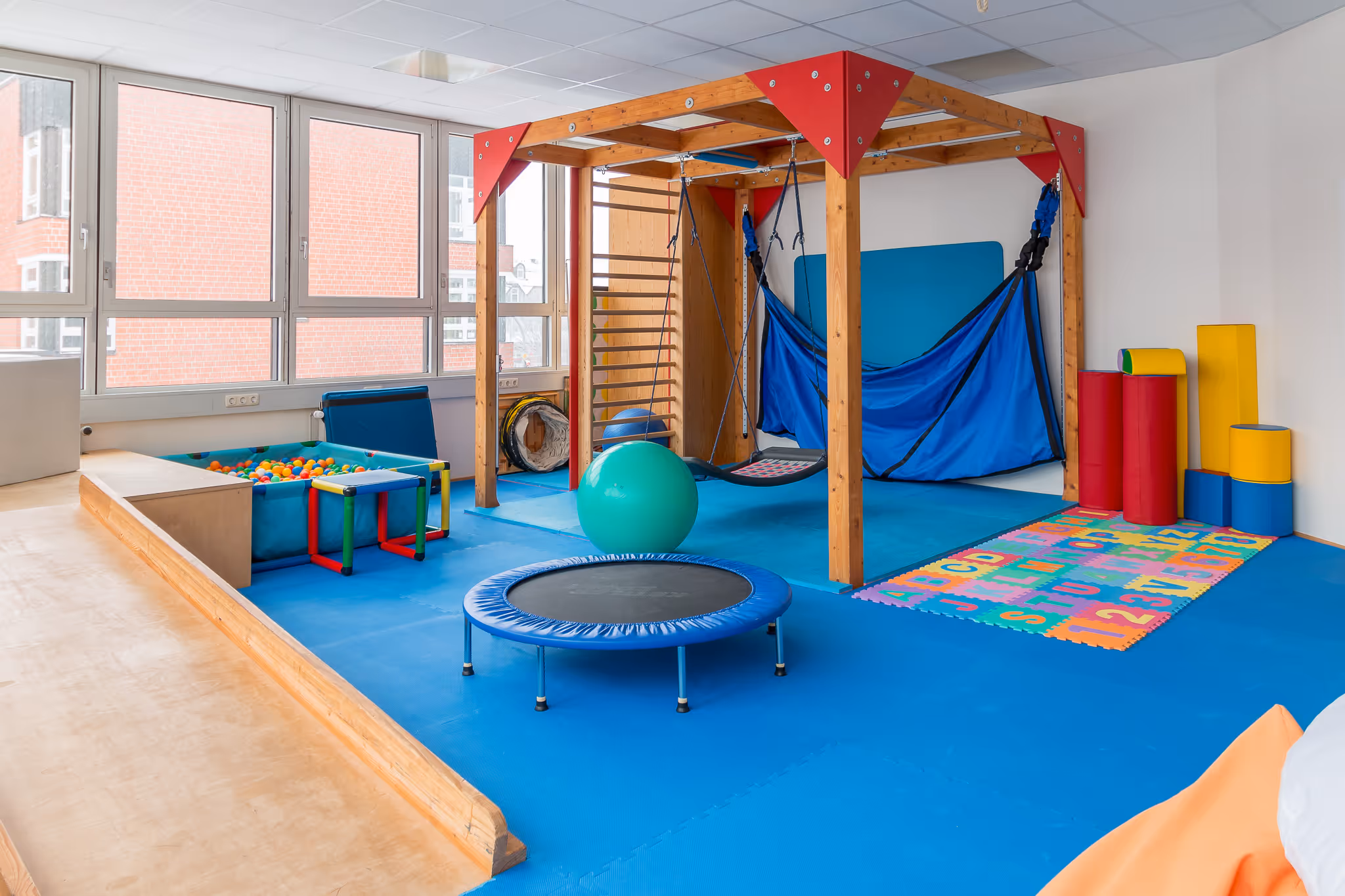 Ergotherapie-Raum für Kinder mit Kletter- und Bewegungslandschaft, Trampolin, Bällebad und sensorischem Therapiebereich