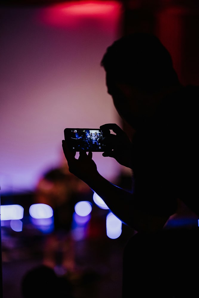 Silhouette d'une personne tenant un smartphone pour filmer un concert avec lumière bleue et rouge en arrière-plan.