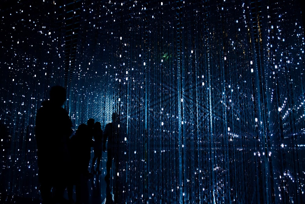 Silhouettes de personnes marchant dans une installation immersive de lumières bleues scintillantes suspendues.