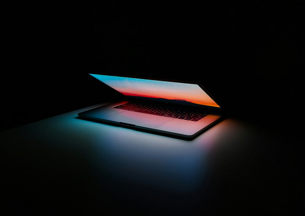 Ordinateur portable partiellement ouvert illuminant une surface sombre avec une lumière colorée.