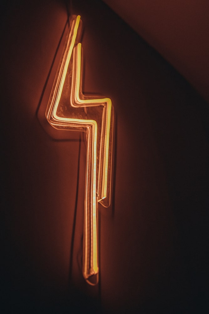 Enseigne au néon jaune en forme d'éclair électrique sur un mur sombre.