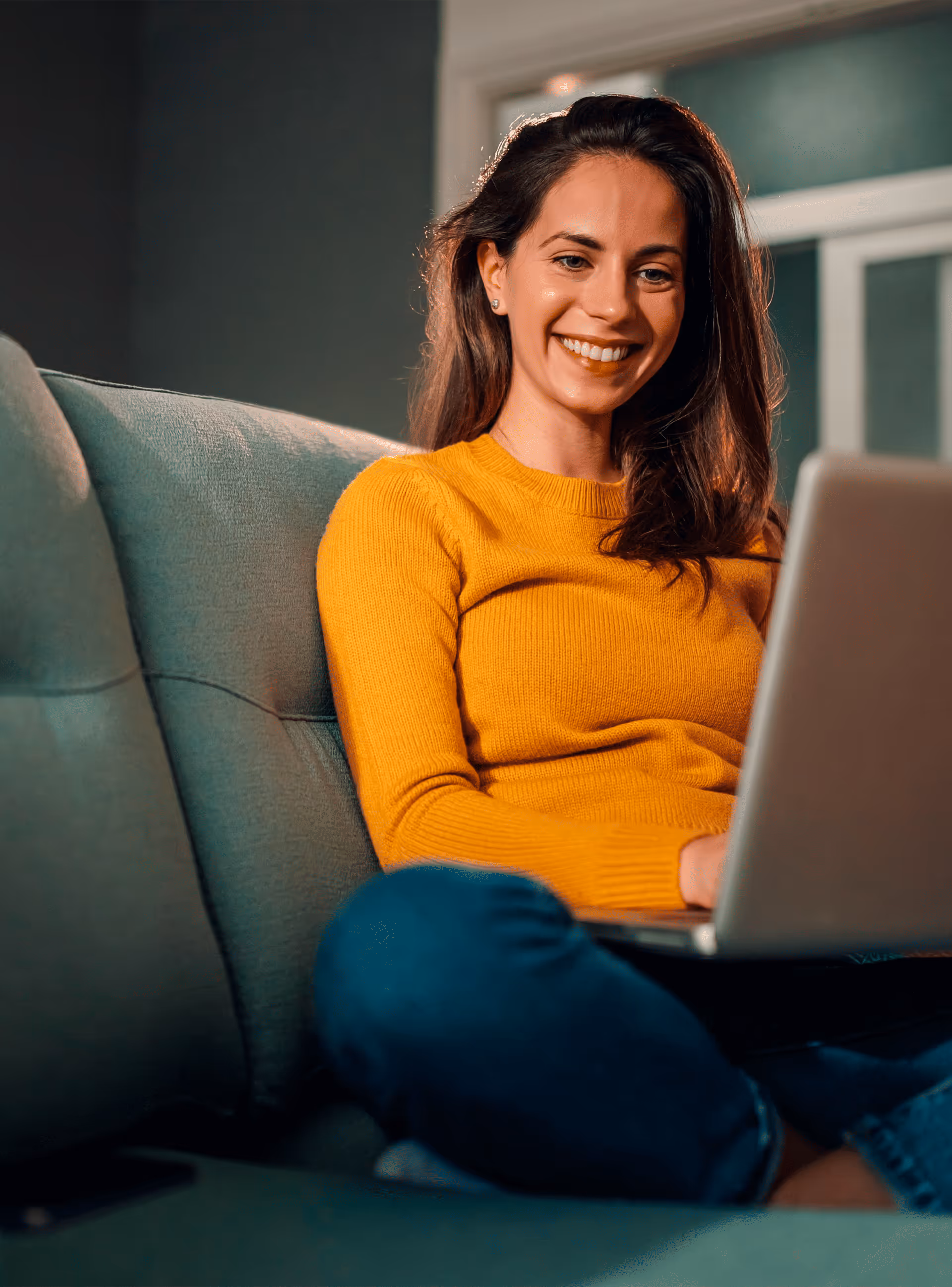 Mulher sorridente sentada no sofá a usar um computador portátil.