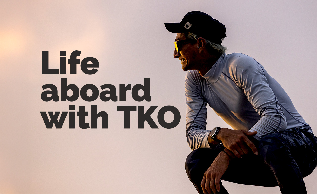 Man in a cap and sunglasses crouching and smiling with text 'Life aboard with TKO'.