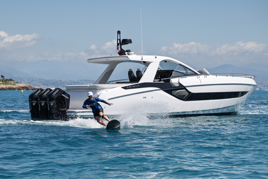 Electric surfing behind a white Azimut motorboat on a sunny day with mountains in the background.