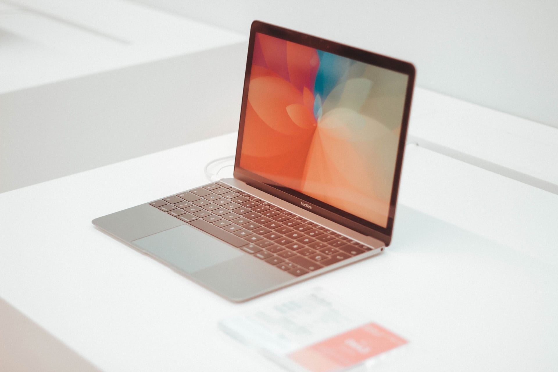 Open silver MacBook on a white surface, displaying an abstract orange and blue wallpaper.