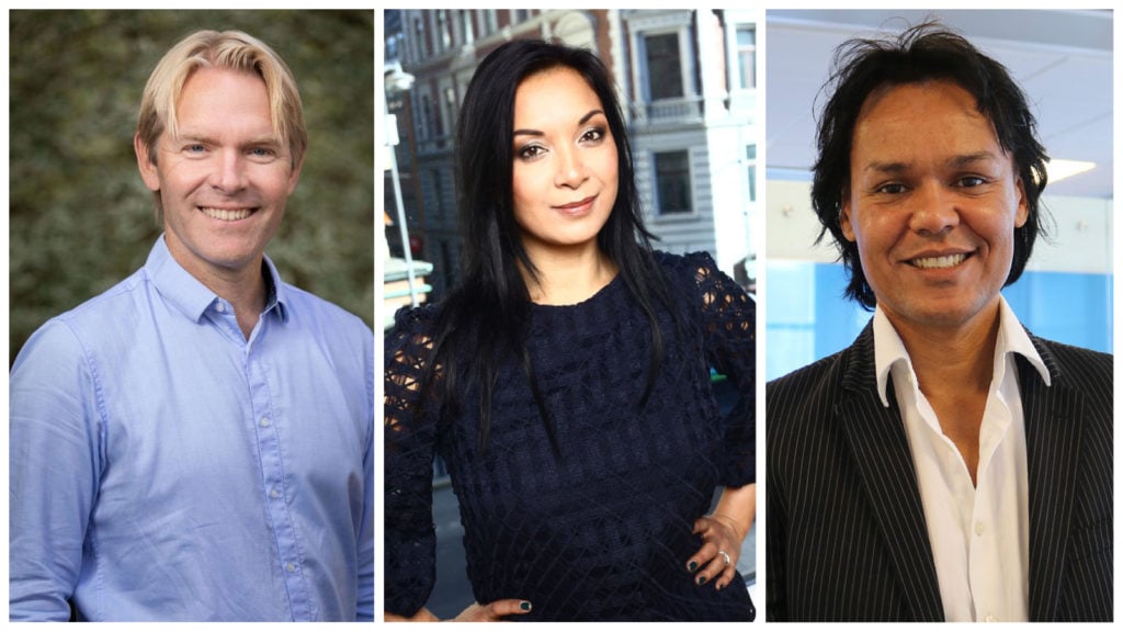 Three smiling people: blond man in blue shirt, dark-haired woman in dark blue lace, dark-haired man in pinstripes.