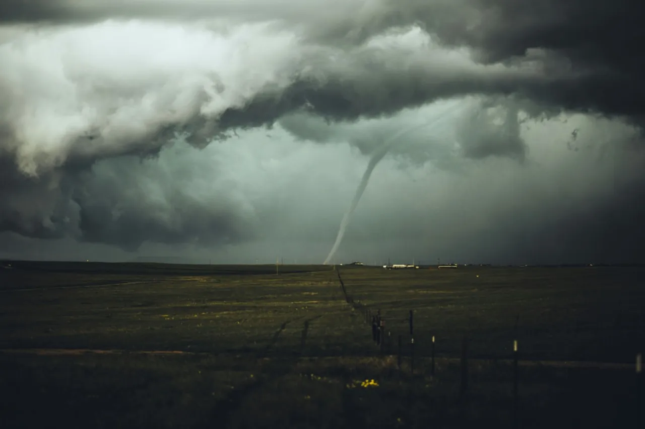Dunkle Gewitterwolken über weiter Landschaft mit sichtbarem Tornado im Hintergrund.