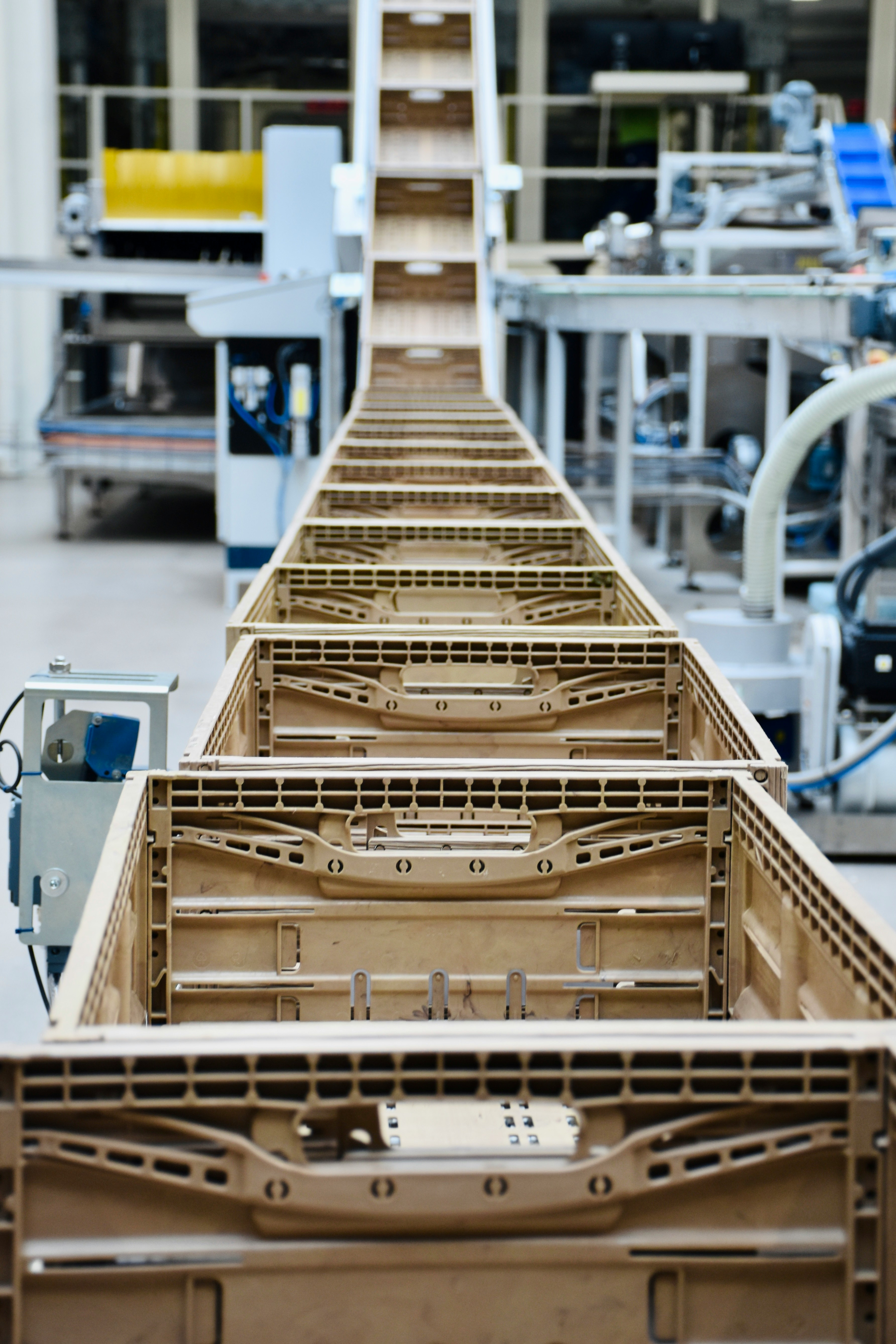 Empty brown plastic crates lined up on a conveyor belt in a factory setting.