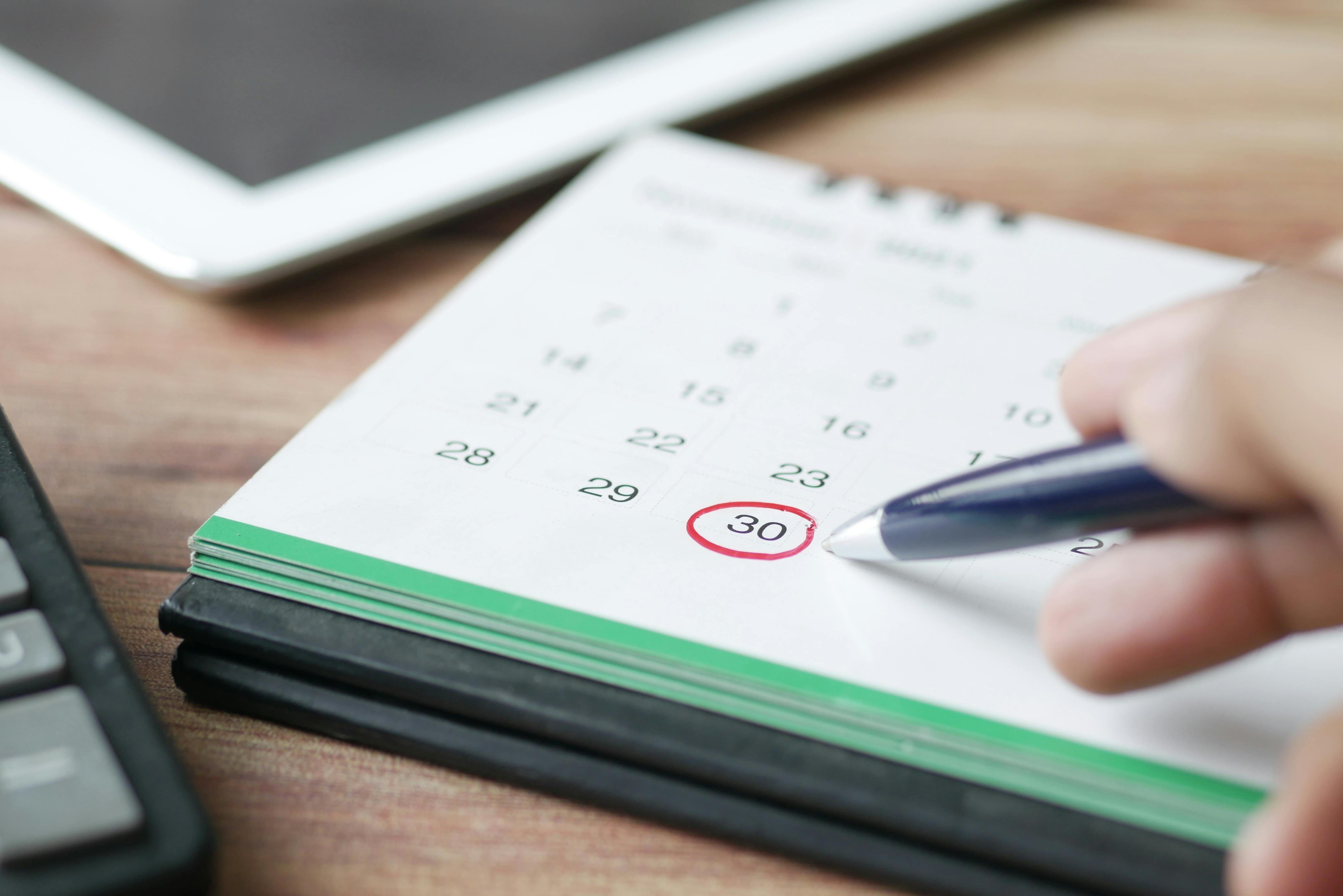 Close-up of a hand holding a pen circling the date 30 on a desk calendar.