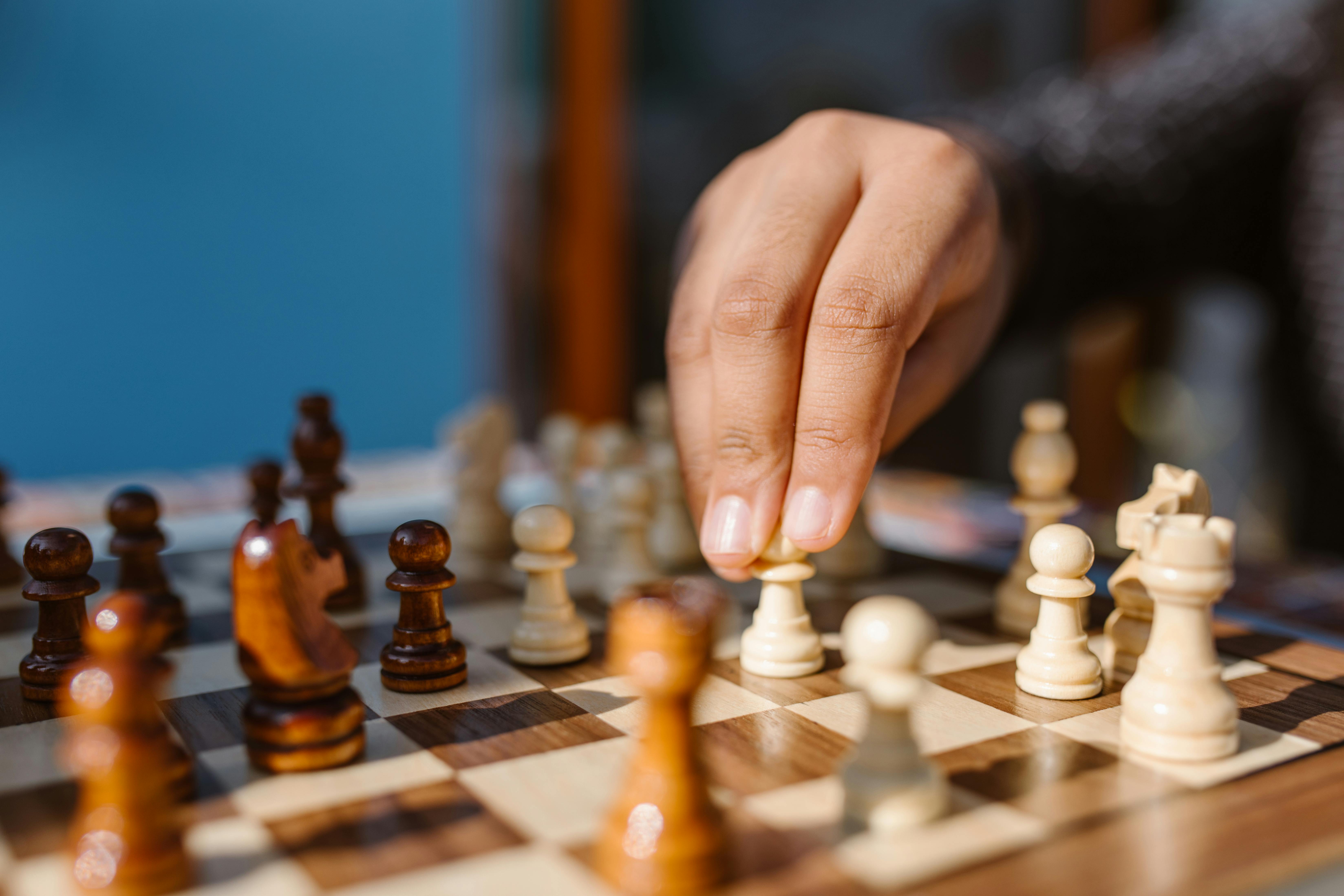 Person moving a white pawn on a wooden chessboard with other chess pieces in focus.