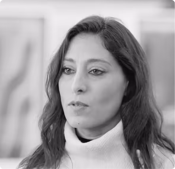 Portrait of a woman with long hair wearing a light-colored turtleneck sweater in an indoor setting.