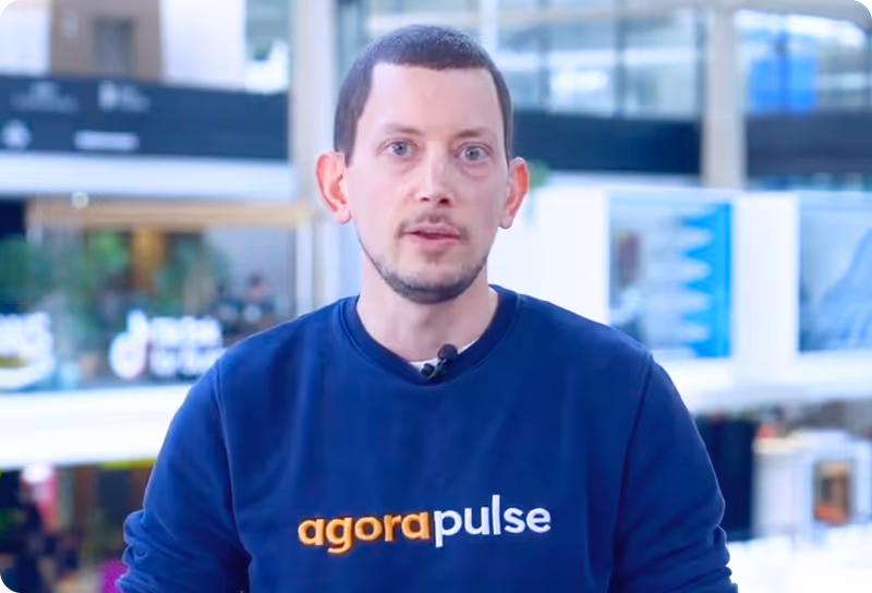 Man with short hair and beard wearing a black Agorapulse sweatshirt speaking in an indoor office setting.