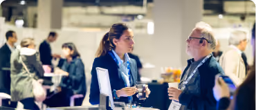 Two people engaged in conversation at a busy indoor event or conference.