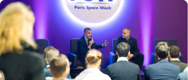 Two men speaking on stage at Paris Space Week with an audience watching in a purple-lit room.