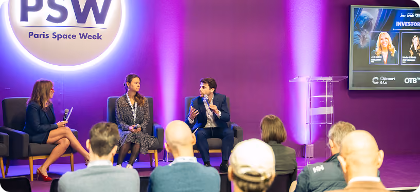 Three panelists seated on stage at Paris Space Week with an audience facing them in a purple-lit room.