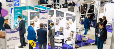 People in business attire talking and walking around booths at a technology trade show.