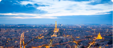 Panoramic view of Paris at dusk with the Eiffel Tower illuminated in the center.