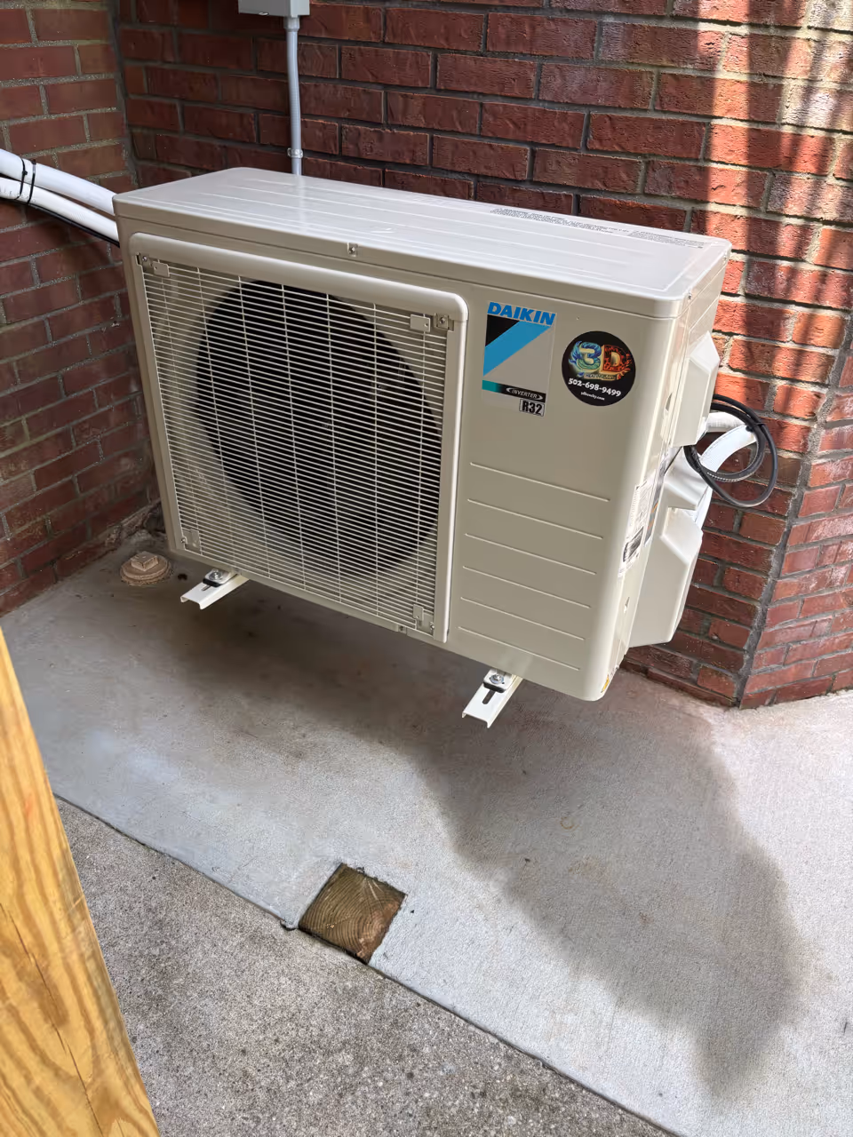 Daikin air conditioning unit installed on a concrete surface near a brick wall.
