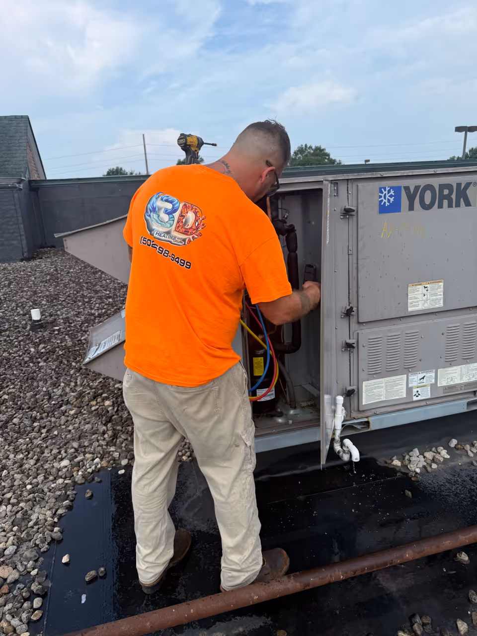 A technician from 3D Heating and Cooling repairs a York HVAC unit on a commercial roof.
