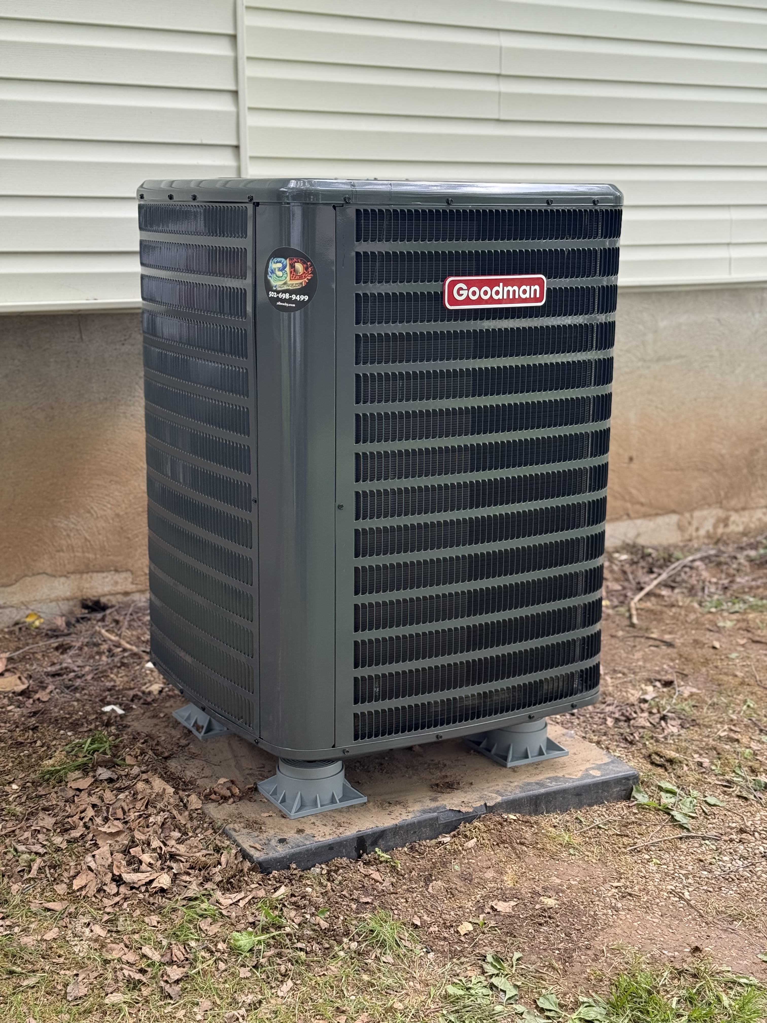 Goodman air conditioning unit installed outside a home, surrounded by grass and leaves.
