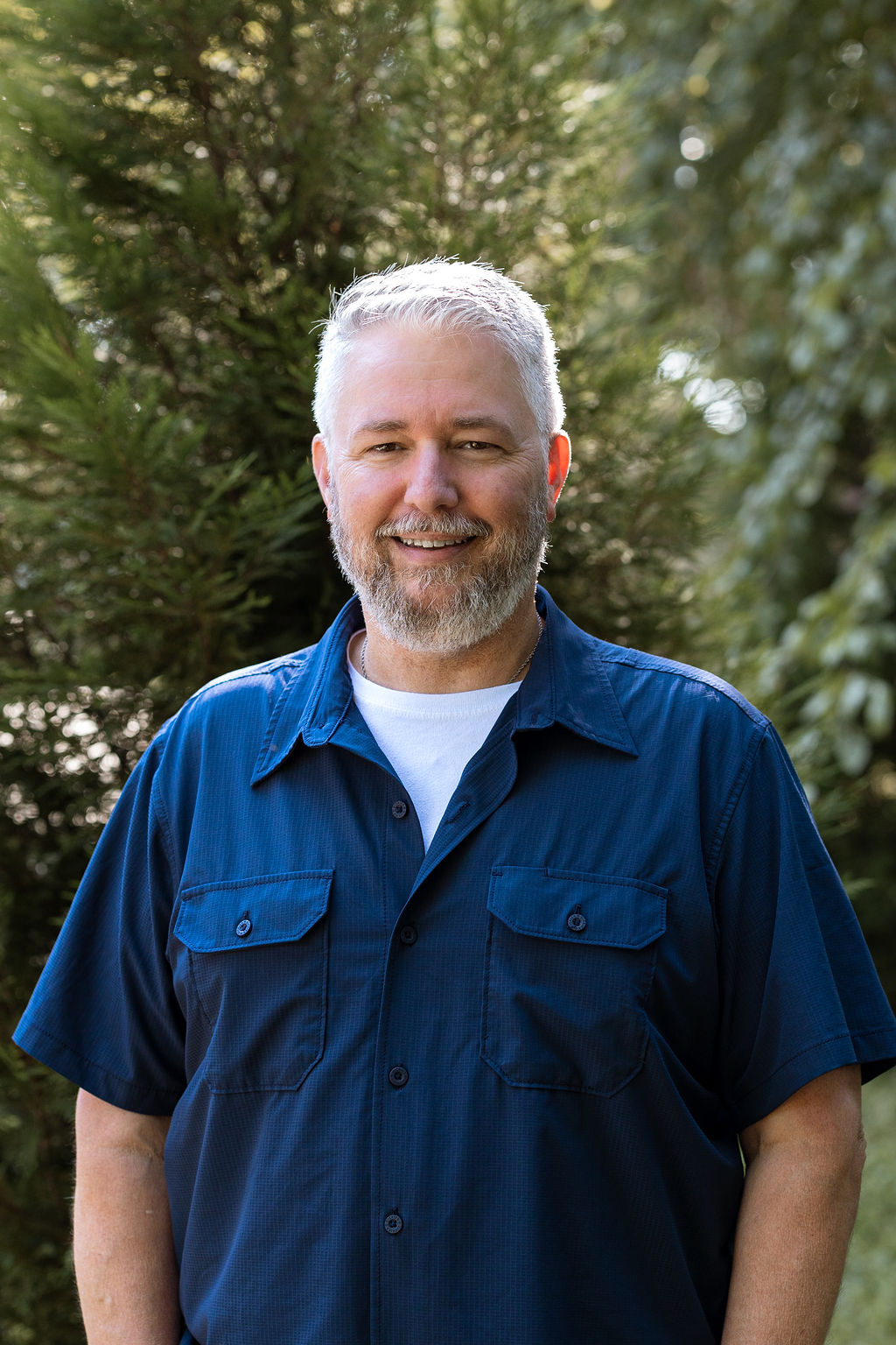 Tim, office manager and webmaster at St. Joseph Tree Service, smiling outdoors in a navy blue shirt.