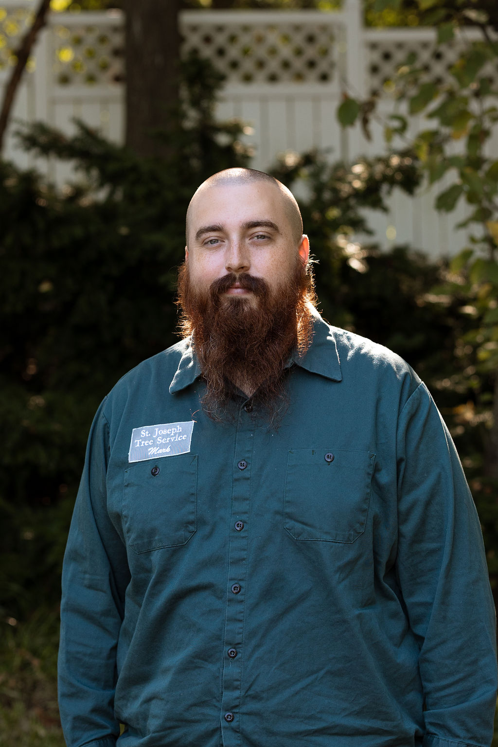 Mark, a member of St. Joseph Tree Service's supporting staff, wearing a teal work shirt with a St. Joseph Tree Service name badge.