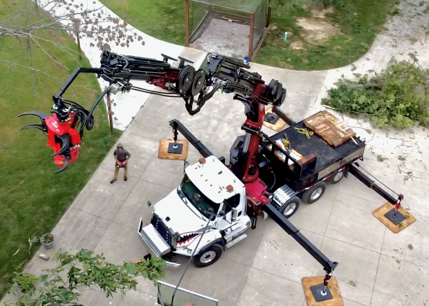 Aerial drone view of St. Joseph Tree Service's BIK 112 grapple saw crane truck with its arm and grapple extended near a job site.