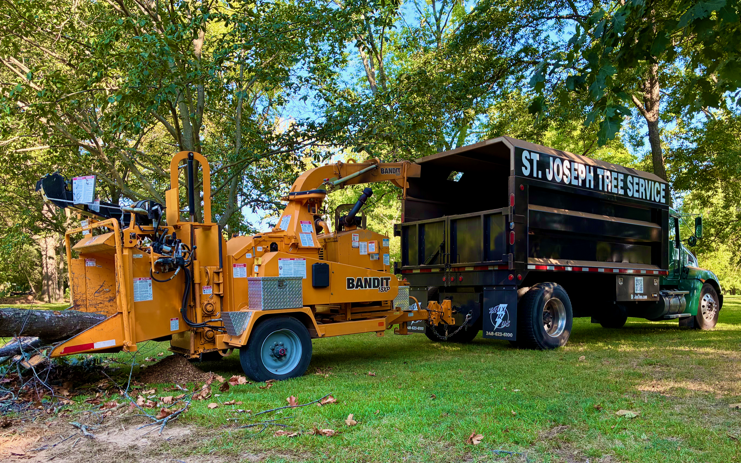 Yellow Bandit 18XP chipper hitched to the St. Joseph Tree Service branded truck, parked in a wooded yard.
