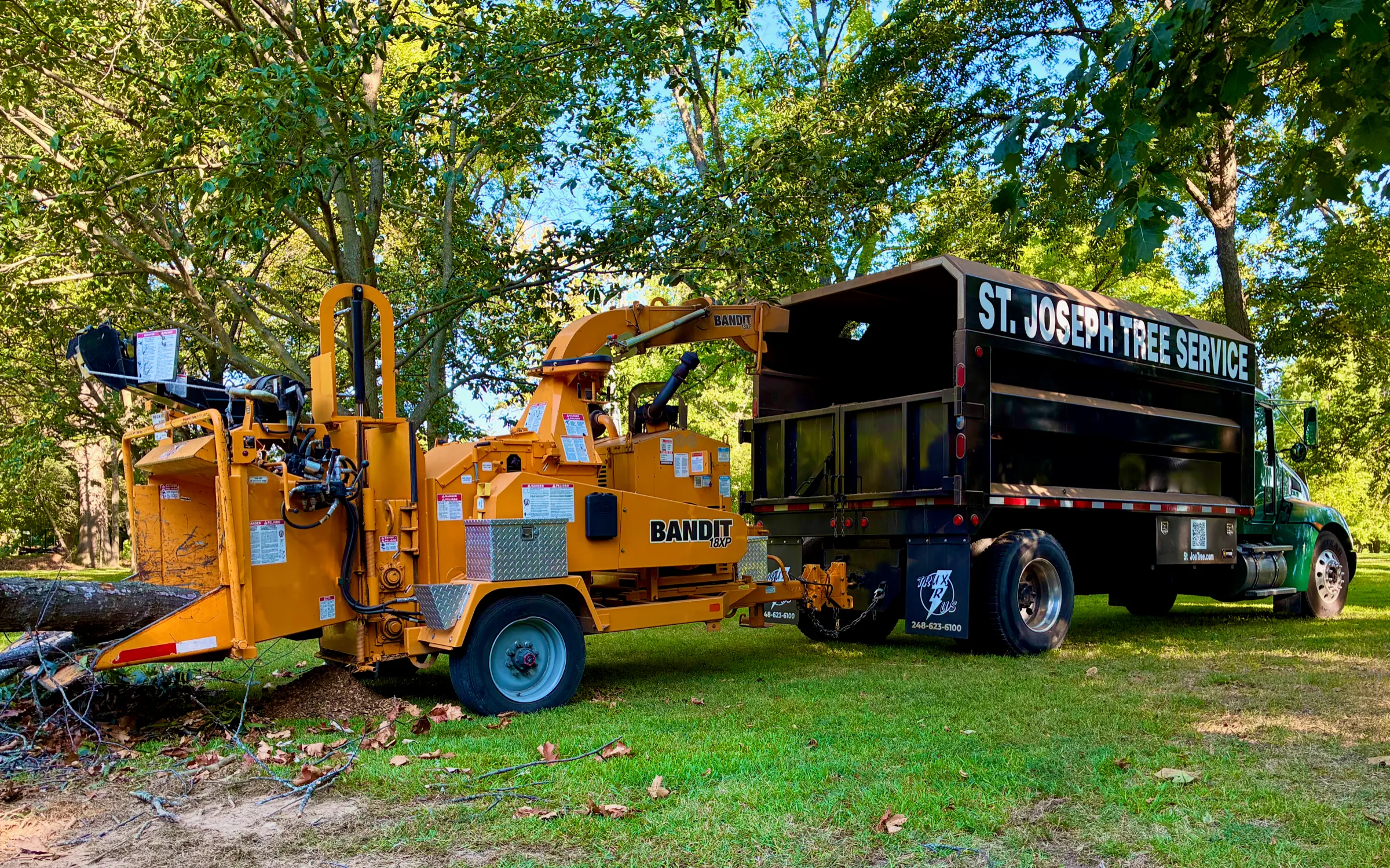 Yellow Bandit 18XP chipper hitched to the St. Joseph Tree Service branded truck, parked in a wooded yard.