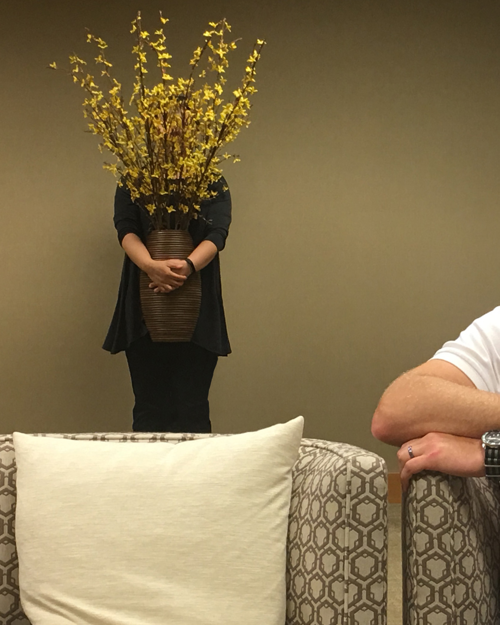 A person holding a large vase of forsythia hiding behind the flowers.