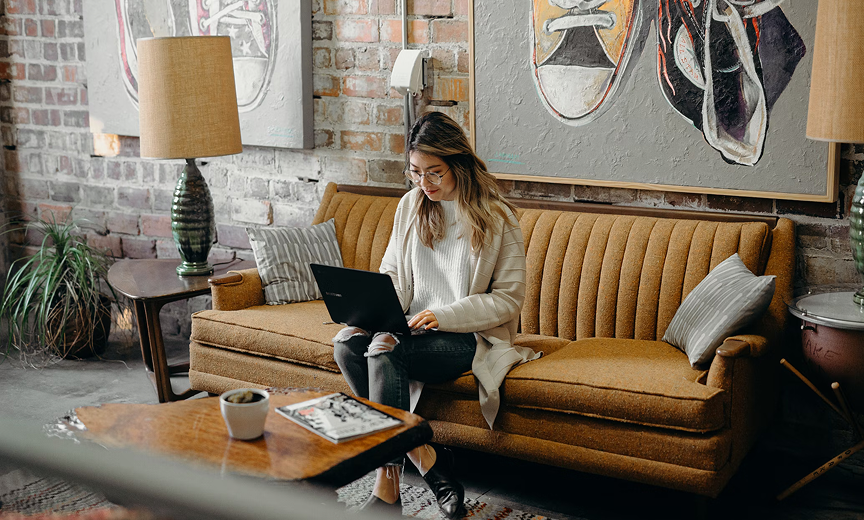 a woman sitting on a beige couch looking at a laptop computer