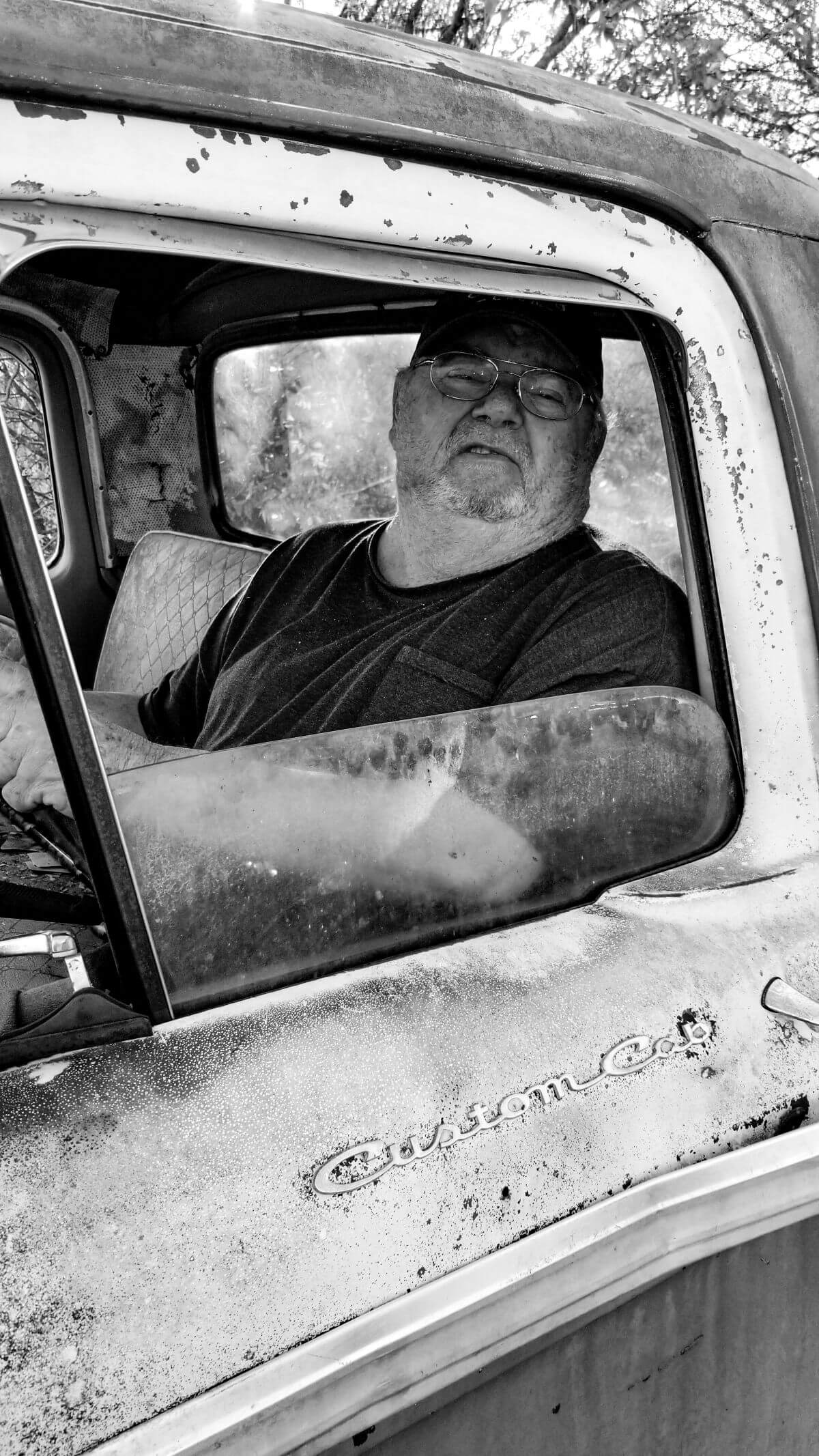 Older man looking out of a old pickup truck window, in black and white.