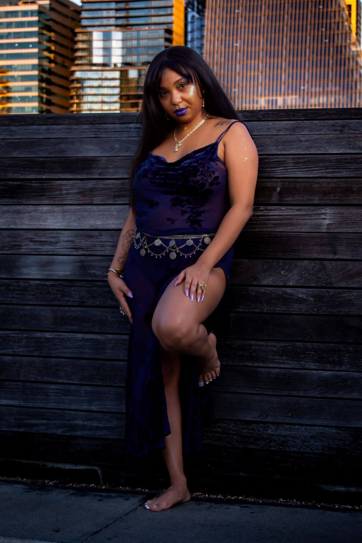 Woman leaning against wooden wall in blue dress. Downtown Austin behind her.