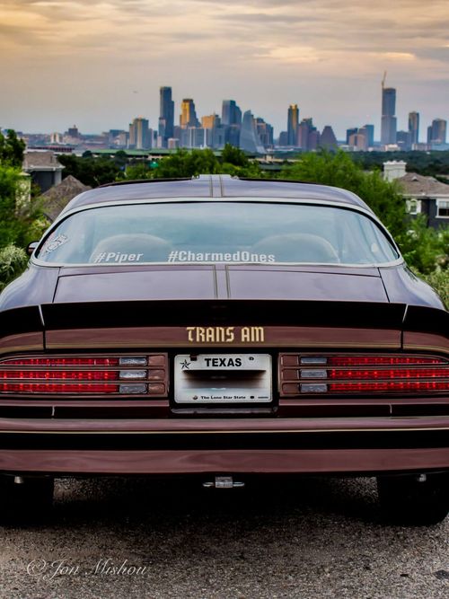 Rear view of a 1977 brown Trans Am, Austin city skyline in the background at sunset.