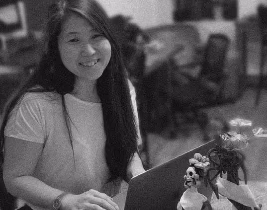 Jee Han smiling at the camera while working on her laptop on a table with flowers