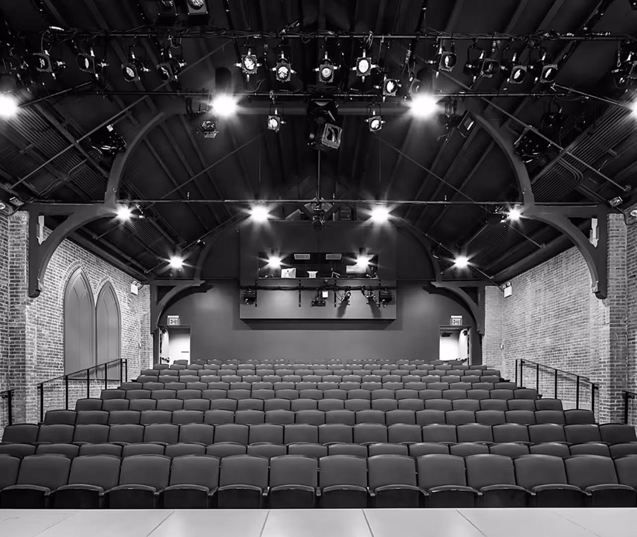 a black & white photo of a theater with raked seating taken from the stage