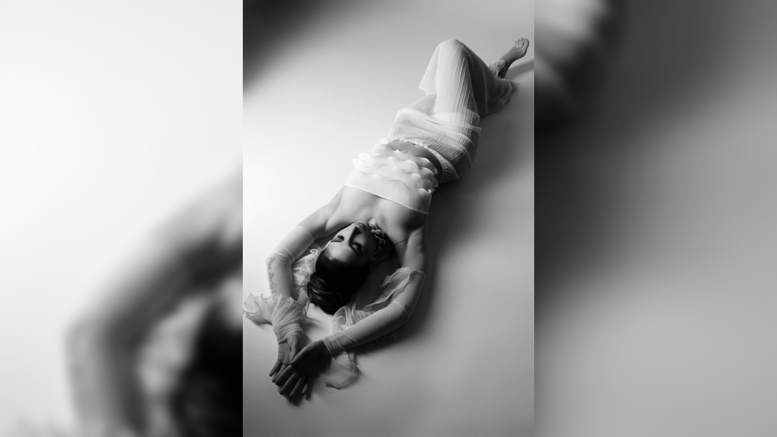 Foto glamour creative portrait di Claudia Spaziani, fotografa fine art a Bologna, modella distesa in posa elegante con abito mesh, luce morbida e superficie riflettente.